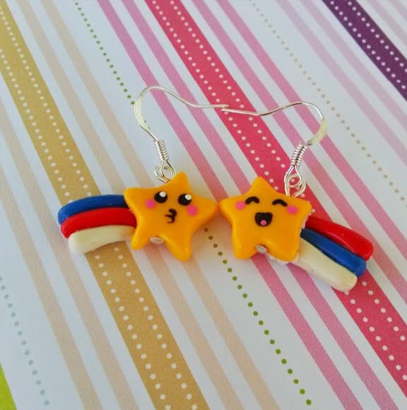 Pair of handmade polymer clay shooting star earrings with rainbow tails on a striped background